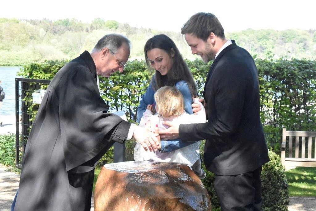 Propst Peter Barz (li.) bei einer Taufzeremonie am Taufstein im Garten im frischen Wasser in Eutin